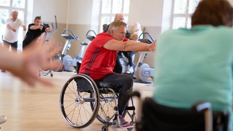 Man i rullstol gör rehabiliteringsövningar i ett gymnastiksal.